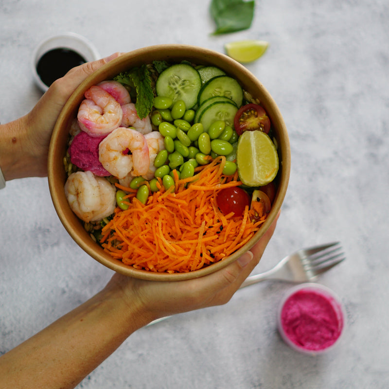 Hand holding a bowl of salad with various ingredients on a marble surface